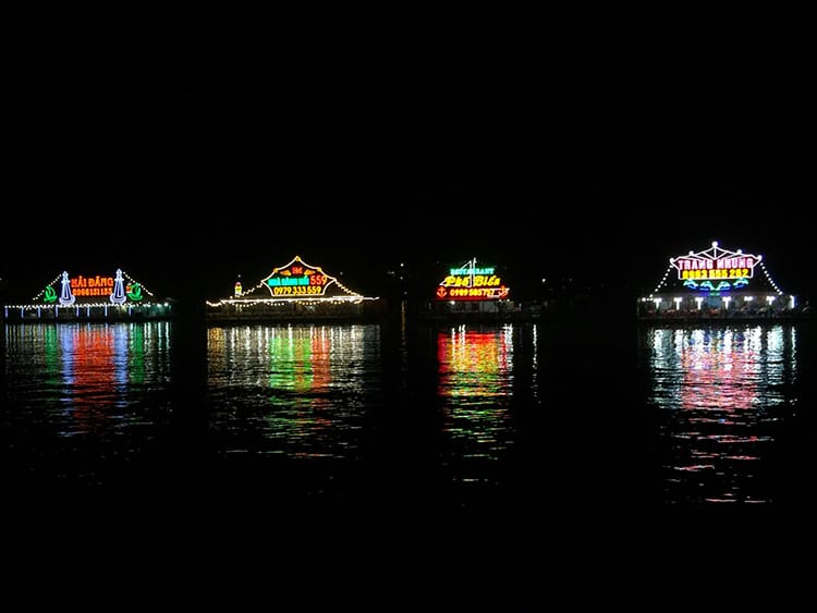 Four karaoke barges float in the water at night with the lights reflecting in the water on Cat Ba Island