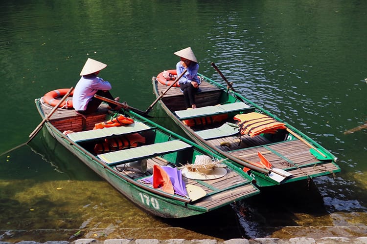 Two boat drivers talk and eat lunch while waiting for tourists at the Trang An Boat Tour in Tam Coc
