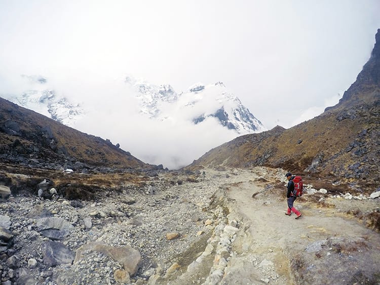 A guide walks on the path down to Khote as clouds roll in across the mountain range