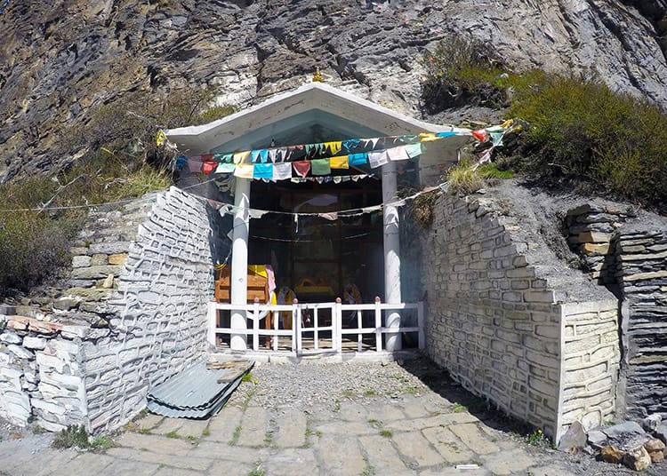 Prayer Flags hang over Milarepas Cave with a religious statue inside