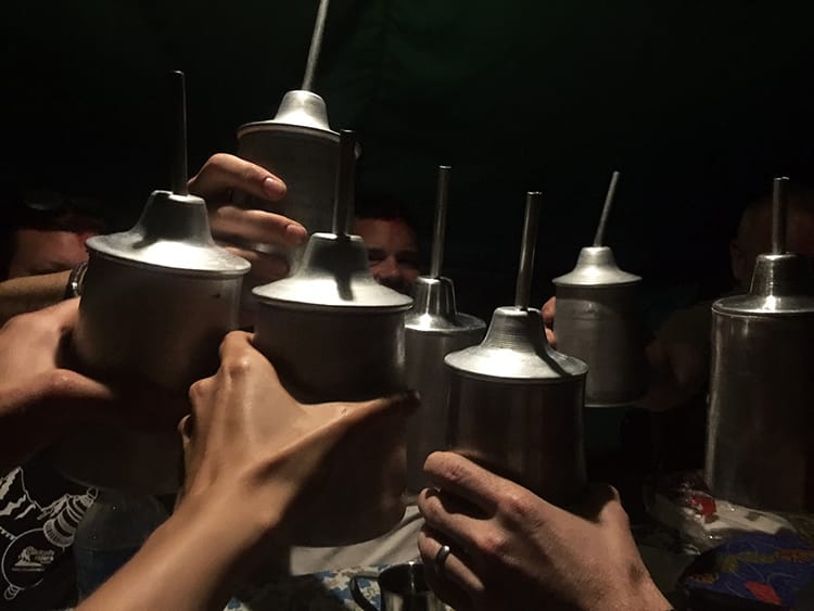 A group of travelers cheers with giant metal mugs of Thongba