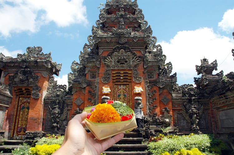 A woman holds an offering of flowers up to a temple in Ubud, Bali