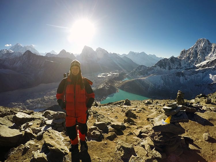 Michelle Della Giovanna from Full Time Explorer stands on a peak near Gokyo Lake where you can barely see Everest