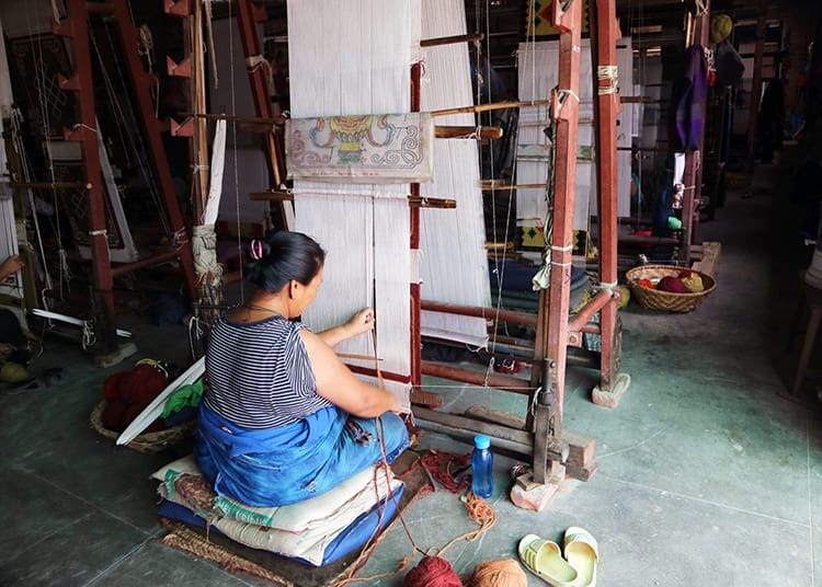 A woman weaves a Tibetan rug by hand on a giant loom