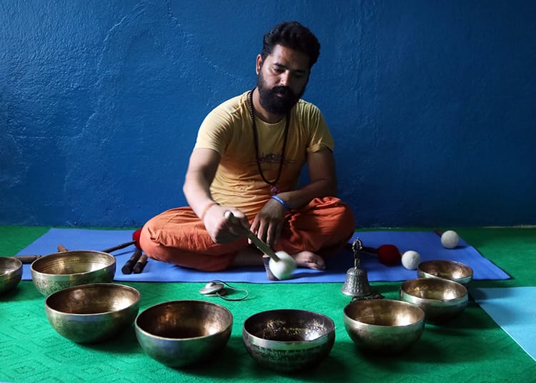 A swami surrounded by singing bowls plays a meditative melody
