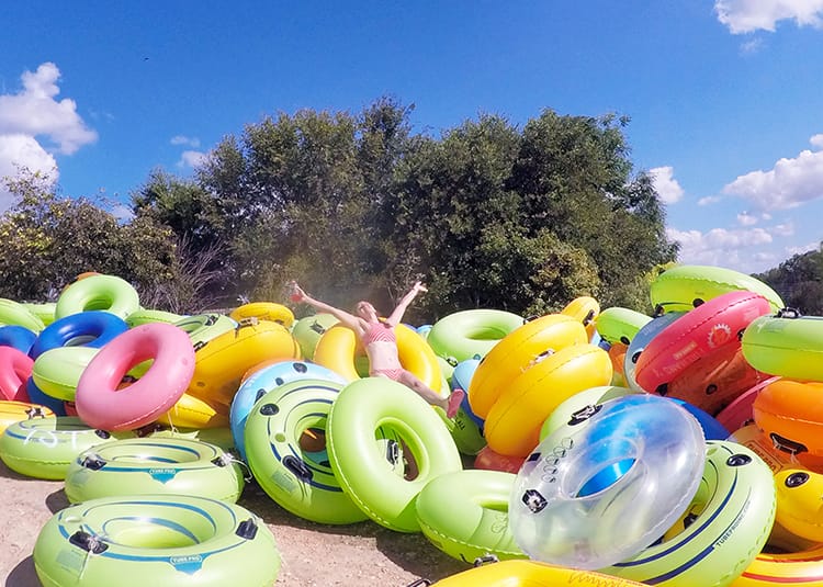 Michelle Della Giovanna from Full Time Explorer sits in a pile of brightly colored river tubes in lime green, yellow, and hot pink