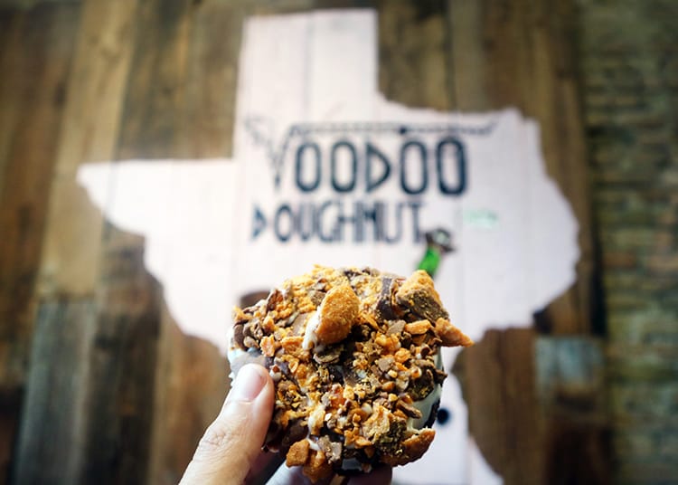 A decadent donut held up in front of the VooDoo donut sign
