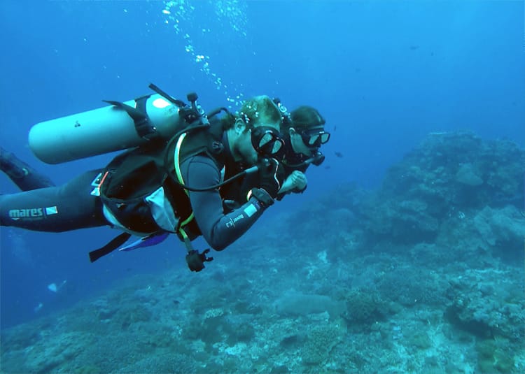 Two scuba divers link arms and swim under water in an assisted dive in Bali