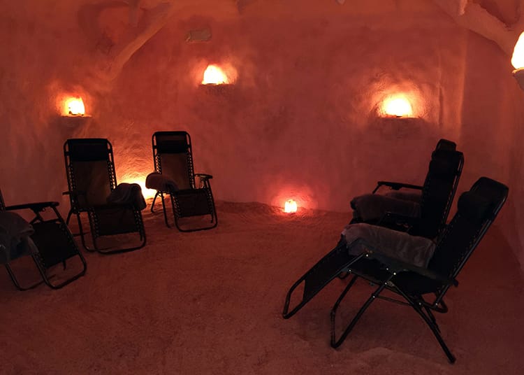 Inside a manmade salt cave with pink walls, Himalayan salt floor, and lounge chairs