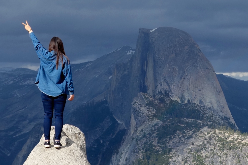 A woman stands on a ledge with an epic view behind her during a day trip to Yosemite