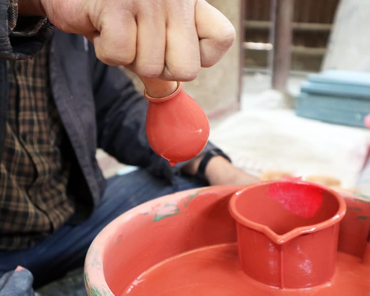 A man dips pottery into glaze and lets the excess drip off