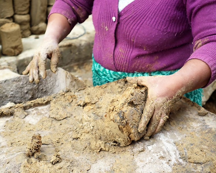 A woman prepares the clay, putting it into a machine to condense it into manageable chunks