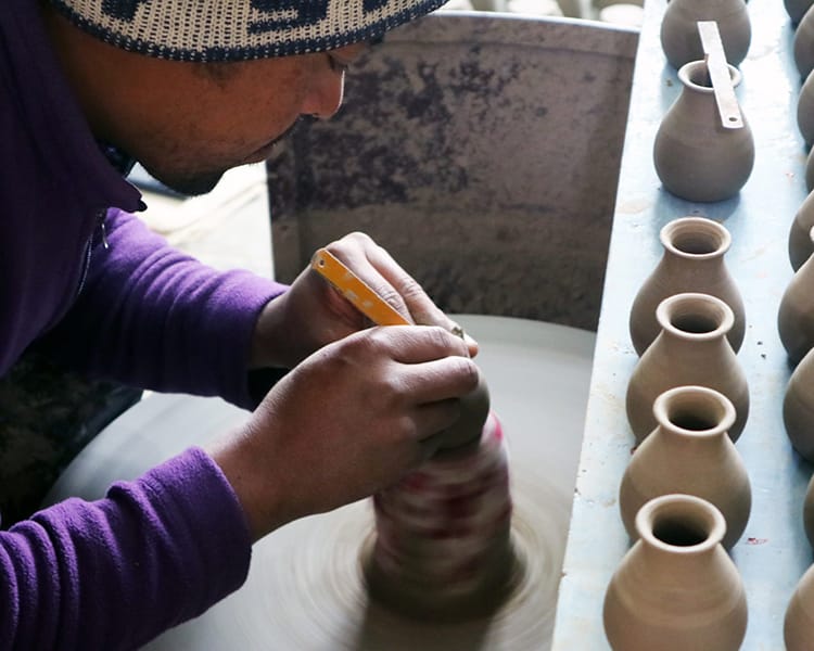 A man makes a small flower vase on a pottery wheel in Thimi