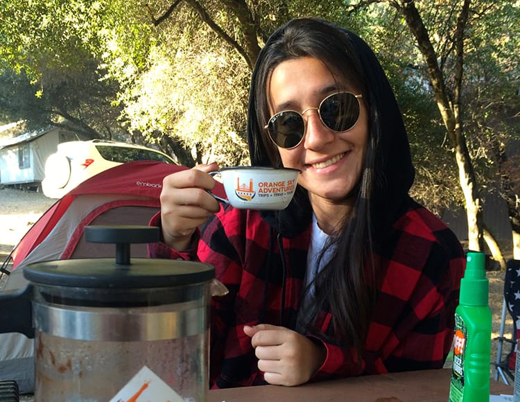 A woman drinks a cup of coffee in preparation for a hike