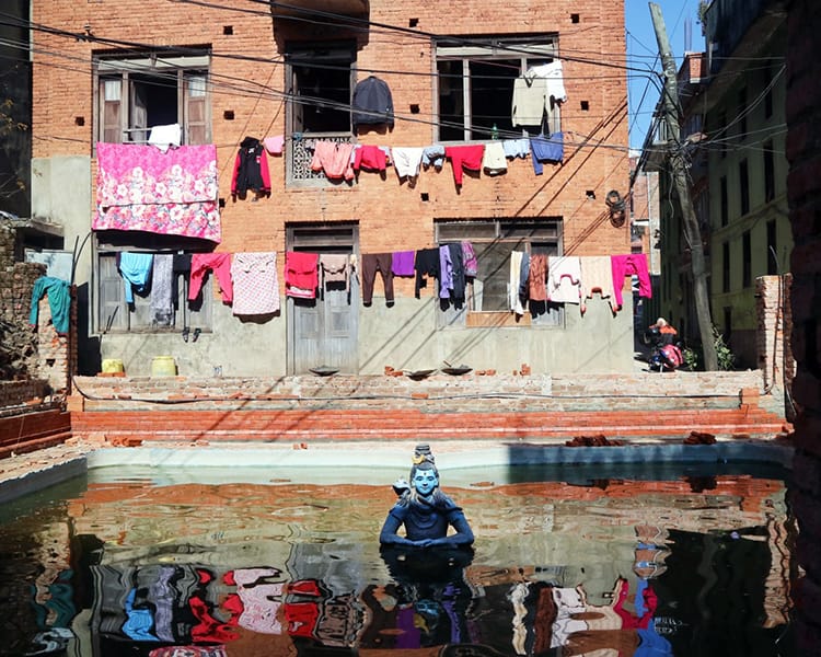 A Visnhu statues sits in a small pond (pokhari) with laundry reflecting in the water in Dhulikhel Nepal