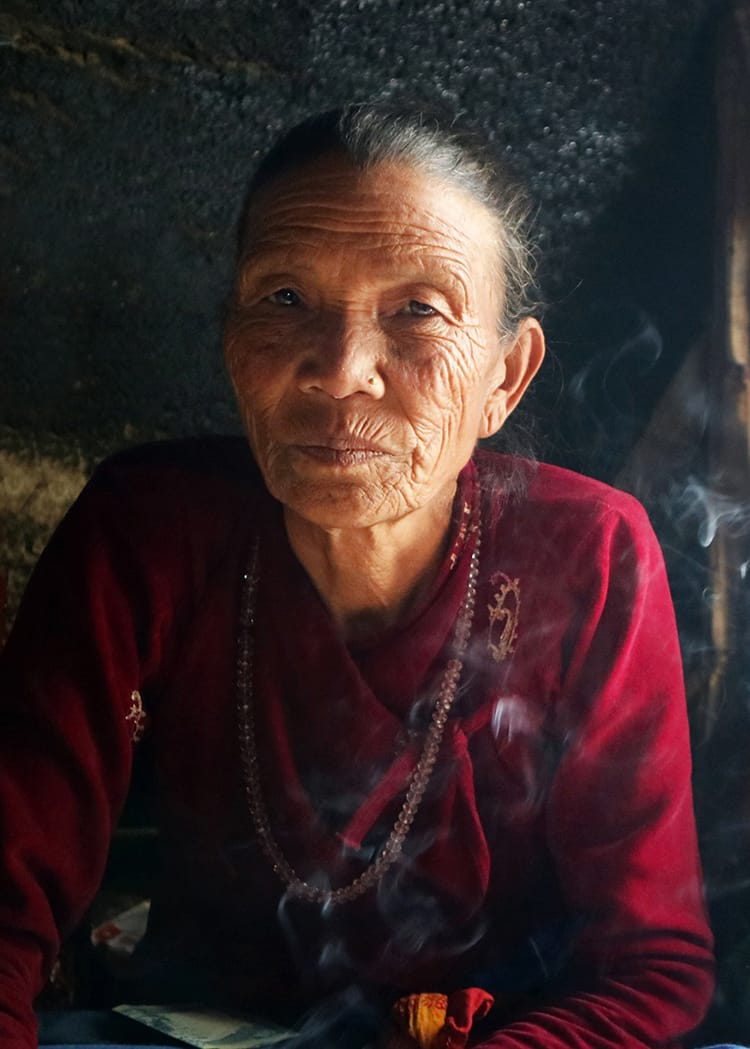 An eldery Tharu woman in Telkot drinks and smokes while talking to us in her teahouse
