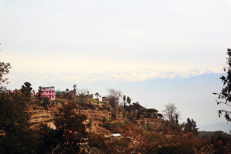 A hot pink house sits on the hillside with the Himalaya in the distance