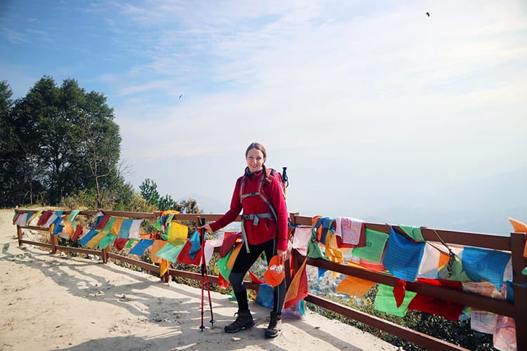 Michelle Della Giovanna from Full Time Explorer stops to take a photo in front of prayer flags on the trekking trail from Dhulikhel to Namo Buddha