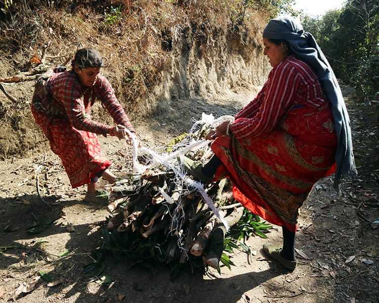 Two women tie a large bundle of wood together before carrying it to their village
