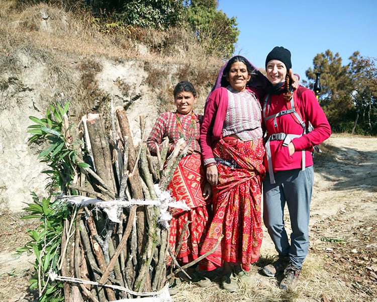 Michelle Della Giovanna from Full Time Explorer stands with two exceptionally strong women carrying wood on their backs