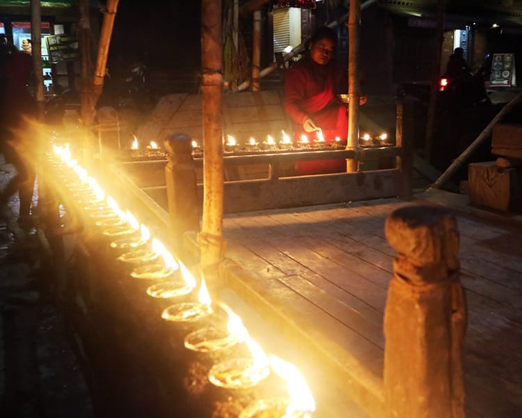 A woman lights candles in the Nyatapola Temple in Taumadhi Square at night in front of the temples