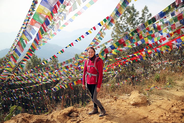 Michelle Della Giovanna from Full Time Explorer stands in front of hundreds of prayer flags while leaving Namo Buddha Monastery in Nepal