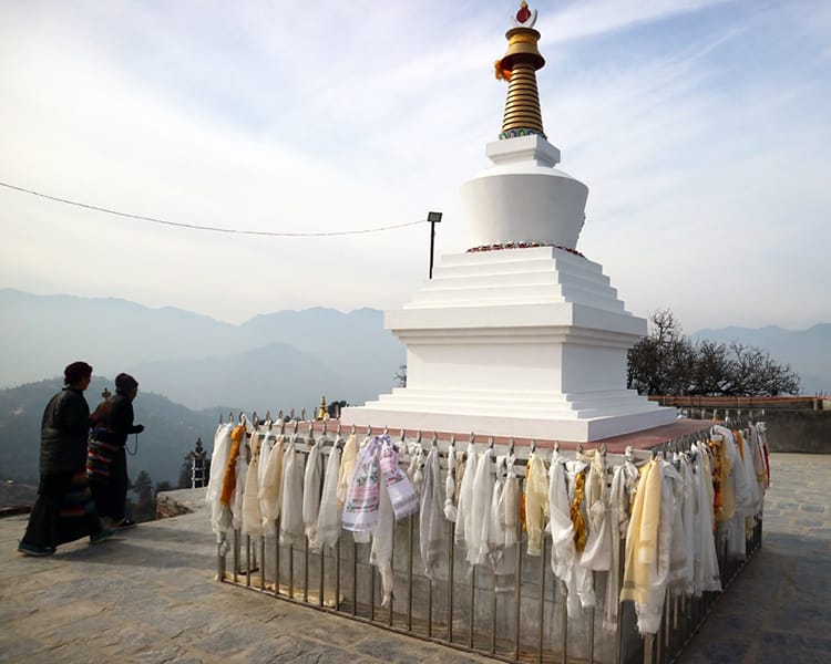 Two women walk around a small stupa at Namo Buddha Monastery while praying