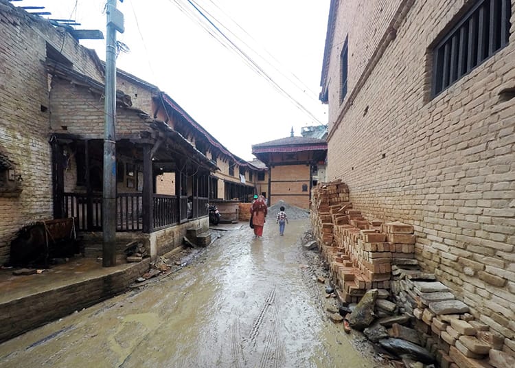 A mother and son walk down a street in Bungamati in the rain