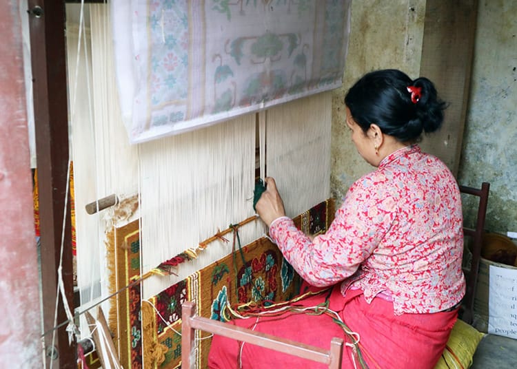 A woman weaves a Tibetan carpet on a loom