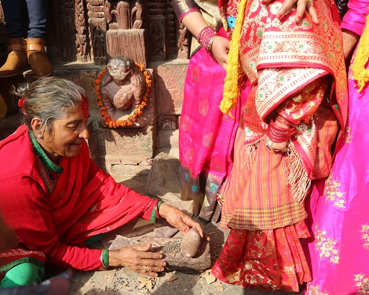 A Nepali woman grinds herbs to apply to the feet of the brides