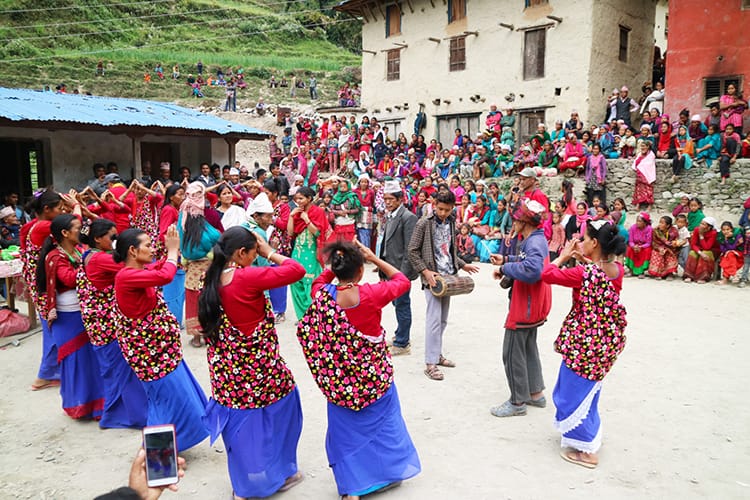 Women wearing purple and red sarees dance with bells on their ankles while singing