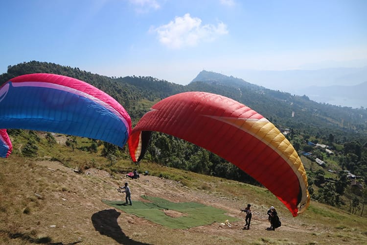 Two pilots line up their parachutes before running off the hill to go paragliding in Nepal