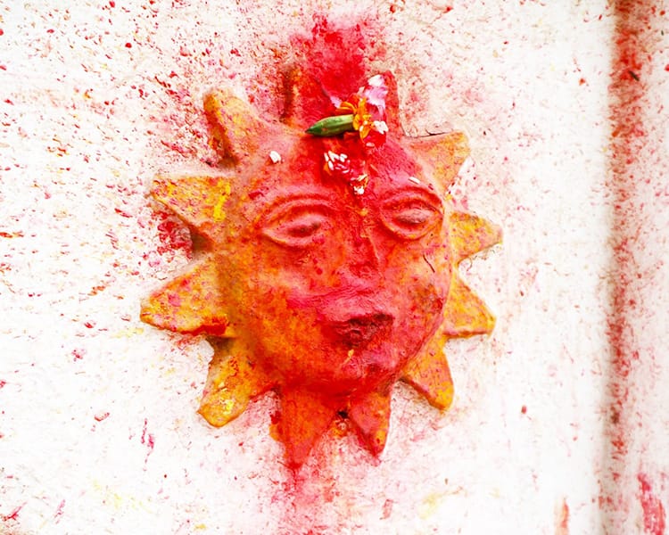 A sun in engraved on the side of a temple and covered in bright orange and red sindoor powder