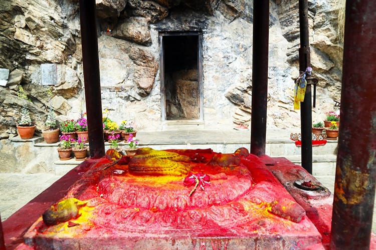 A carving of two feet is positioned in front of Asura Cave and covered in sindoor powder