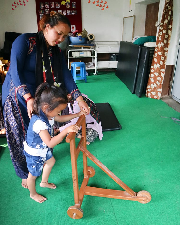 A young girl pushes a wood contraption around to help her learn to walk