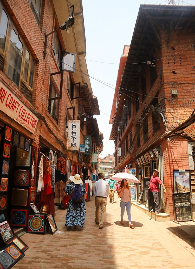 People walk down the streets in Bhaktapur with brick shops and a brick walkway