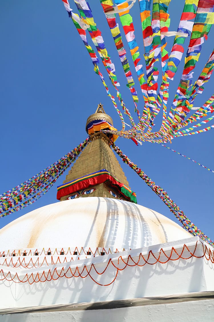 Boudhanath Stupa on a sunny day with prayer flags flying in the wind