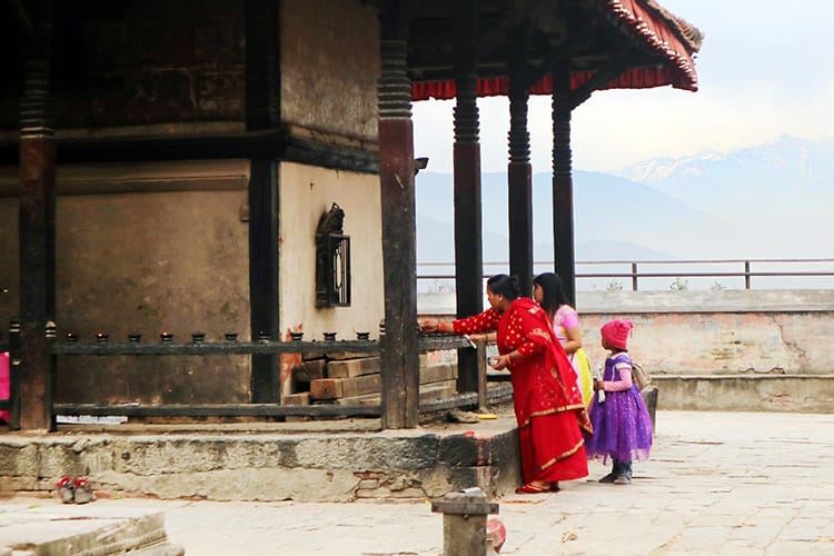 Two women and a young girl perform puja at a temple in Kirtipur