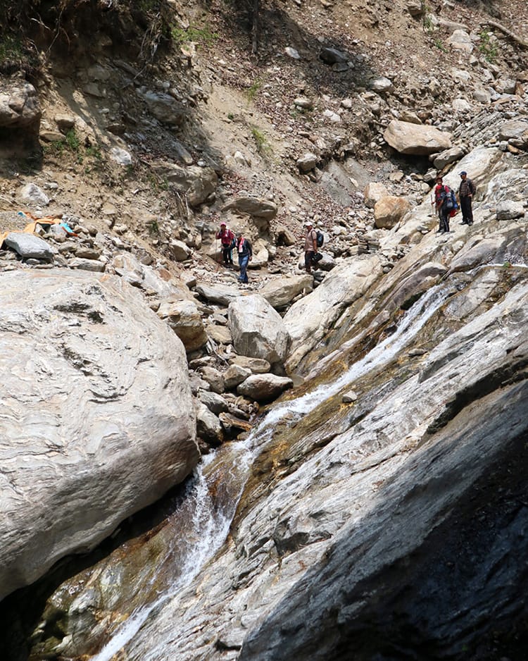 Trekkers climb down a steep rock across a river on the way to Kyalche, Nepal