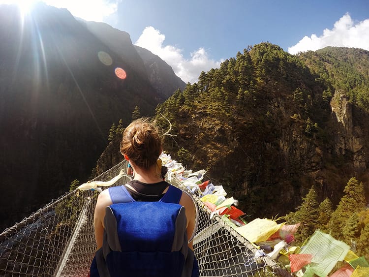 A trekker crosses a suspension bridge on the way to Everest Base Camp while wearing her backpack