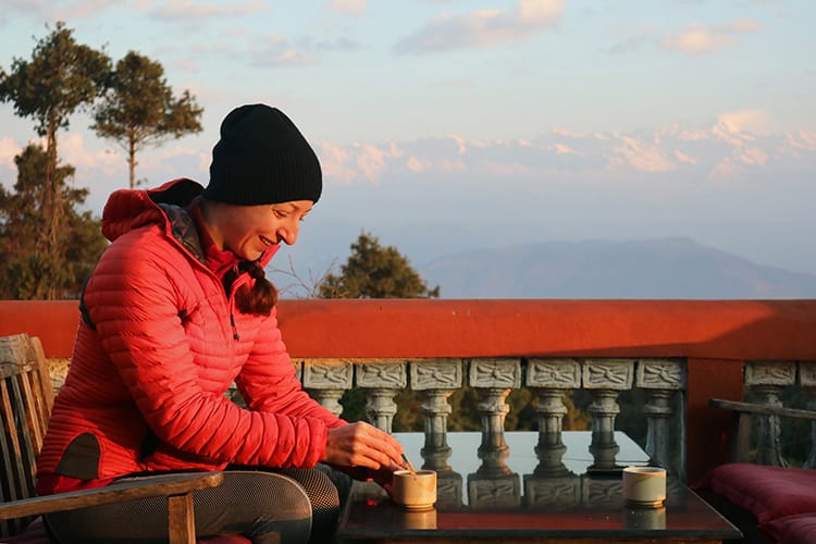 Michelle Della Giovanna from Full Time Explorer sits drinking a cup of coffee while watching the sunrise in Nagarkot