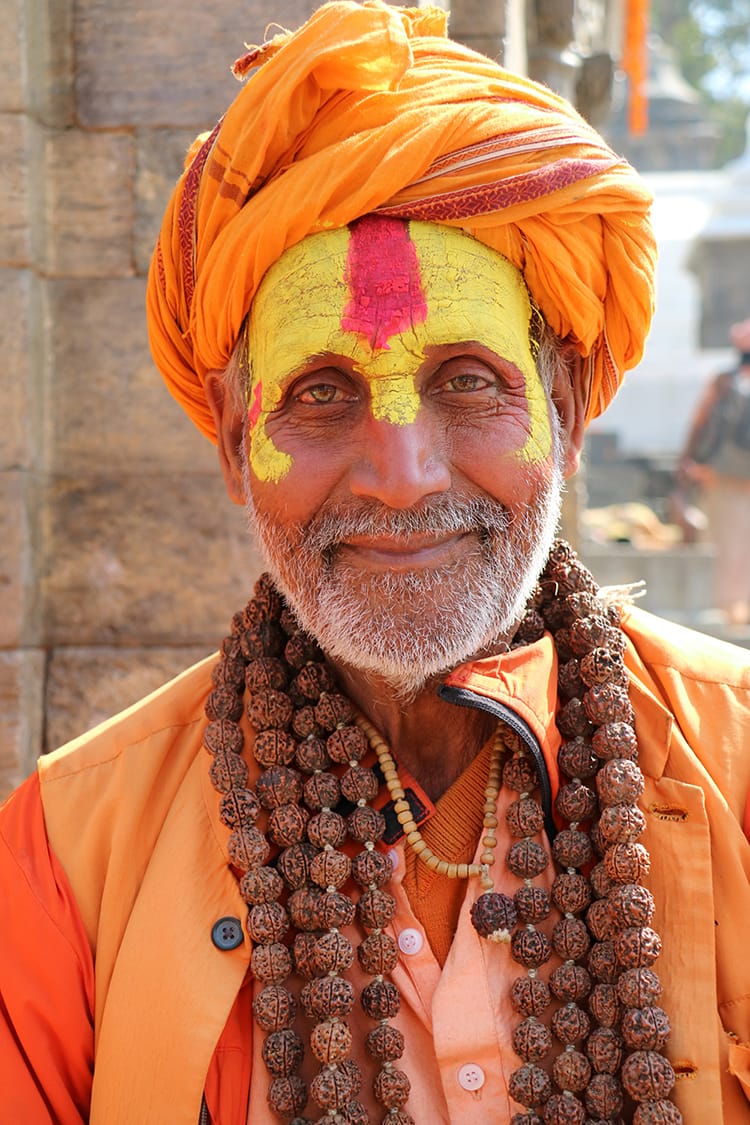 A guru in Pashupathinath Temple wearing an orange turban, face paint, and multiple strands of mala beads during Maha Shivaratri in Nepal