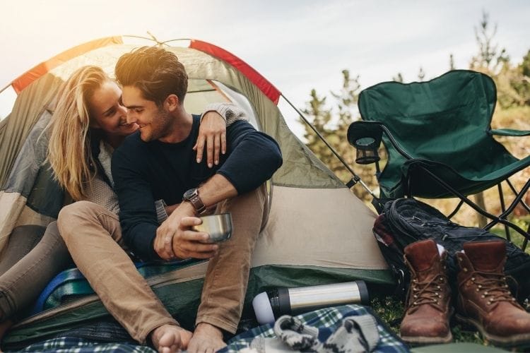 A couple snuggle up and laugh while camping - Travel Inspired Stay at Home Date Ideas for Couples