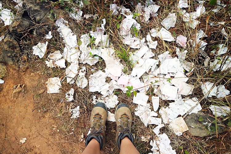 Michelle Della Giovanna from Full Time Explorer stands looking down at trash on the ground on a hiking trail near Pharping, Nepal