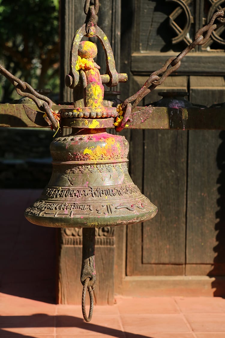 A large brass bell sits outside a temple with sindoor powder on it from worship