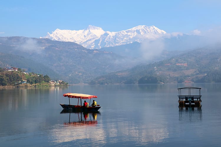 People take a paddle boat out onto Begnas Lake with the Annapurna Range behind them