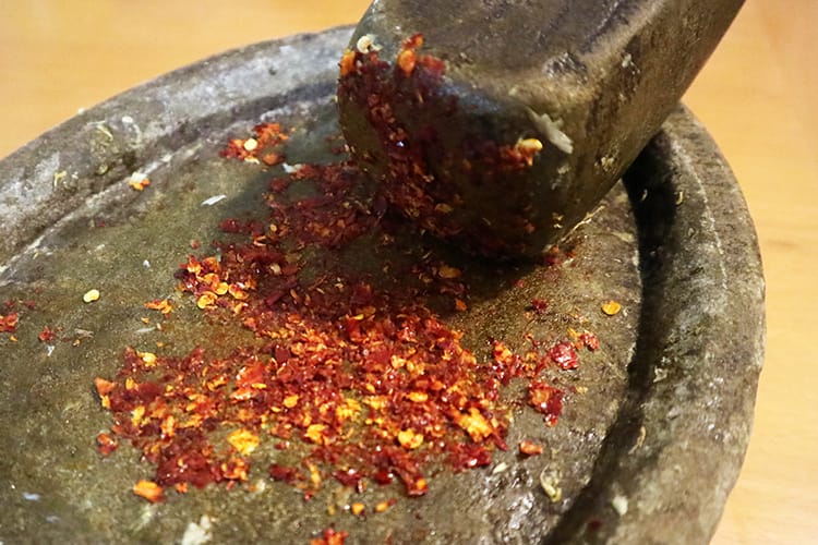 Grinding whole dried chilies with a mortar