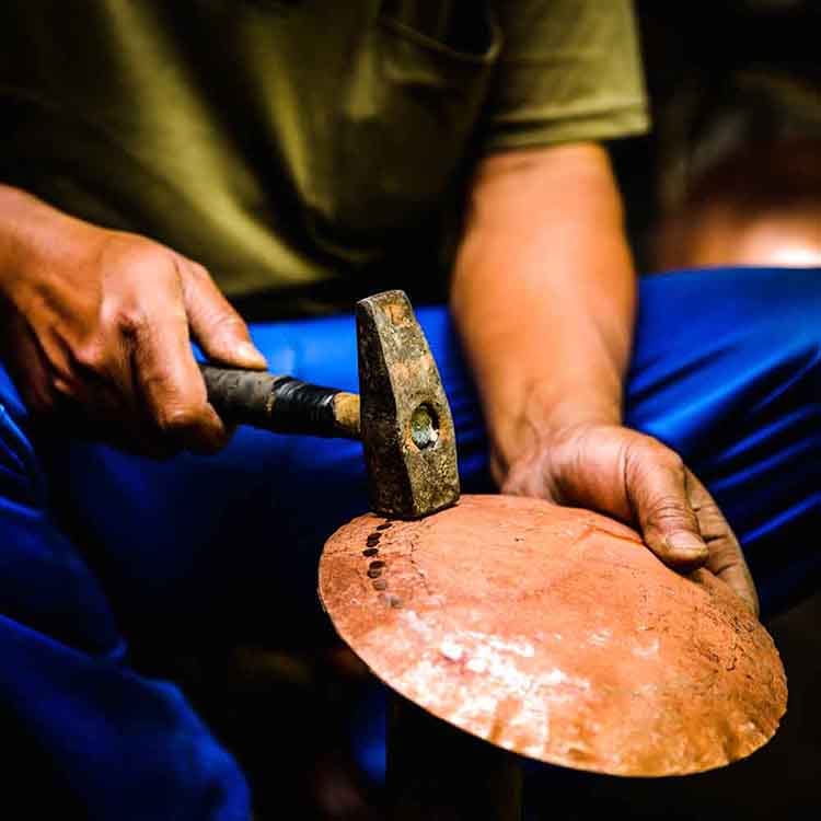 A man hammers a piece of copper into a bowl