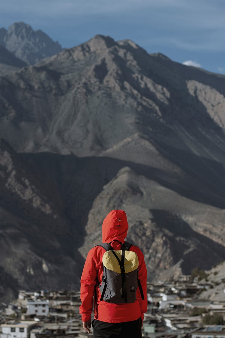 A man stands in front of a mountain wearing a Yatri Supply backpack