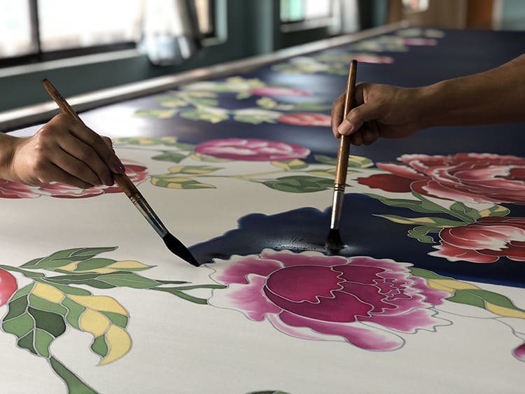 Two people hand paint a piece of silk with large vibrant flowers